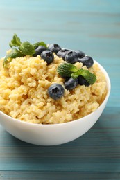 Photo of Tasty millet porridge with blueberries and mint in bowl on light blue wooden table