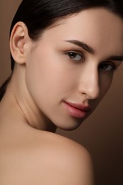 Beautiful young woman with healthy skin on brown background, closeup