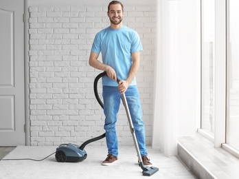 Young man cleaning carpet with vacuum at home