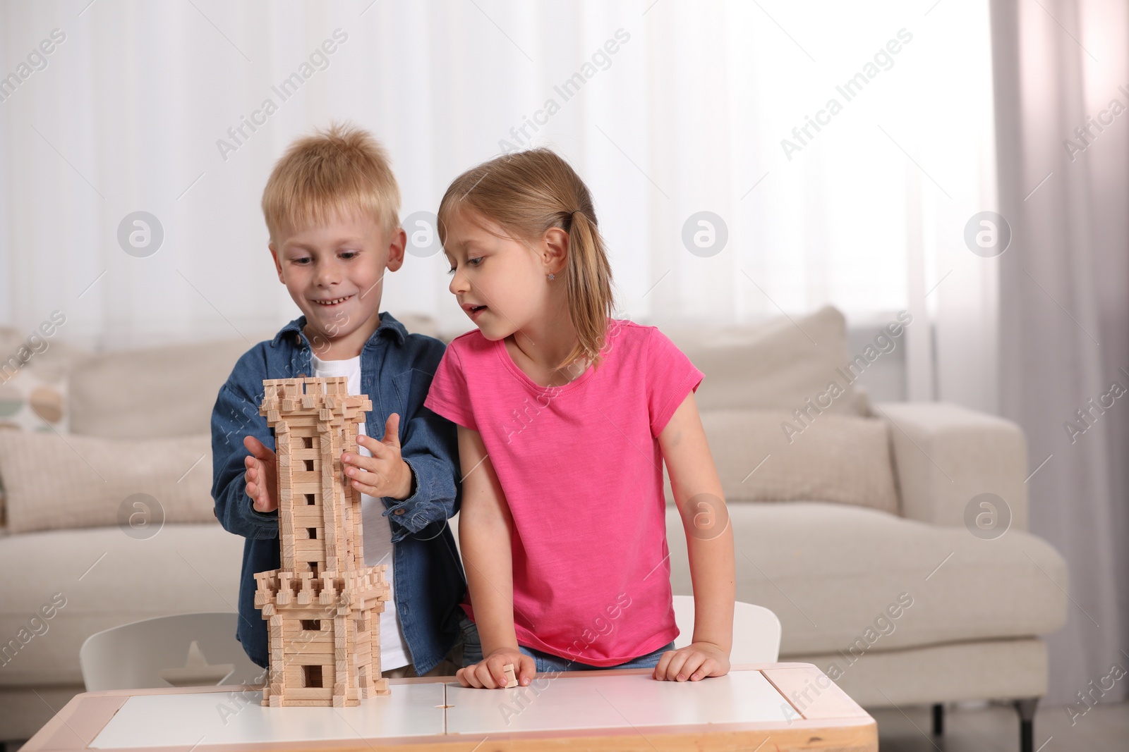 Photo of Little girl and boy playing with wooden tower at table indoors. Children's toy