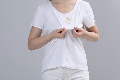 Photo of Woman showing stain on her t-shirt against light grey background, closeup