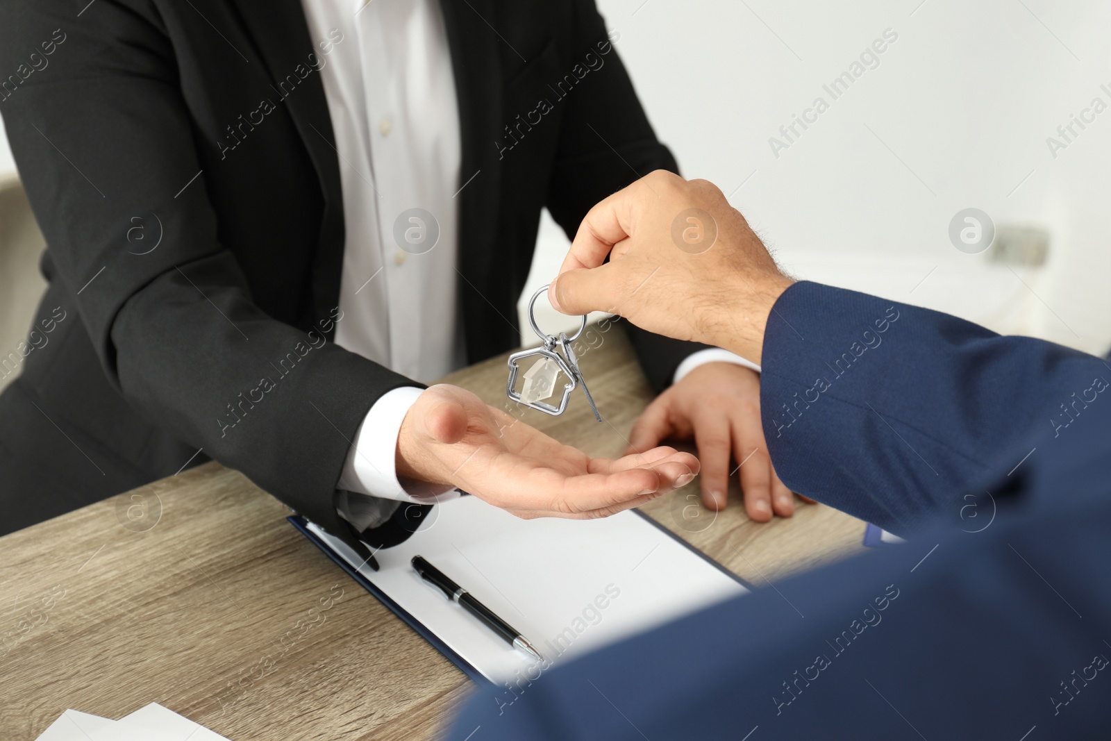 Photo of Real estate agent giving key to client at table in office, closeup