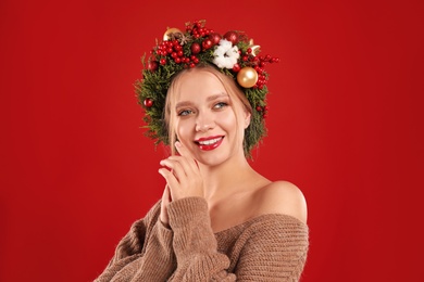 Beautiful young woman wearing Christmas wreath on red background