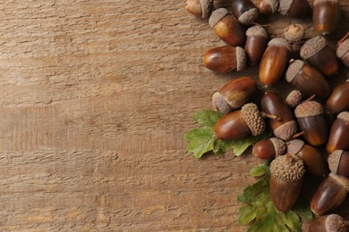 Photo of Acorns and oak leaves on wooden table, top view. Space for text