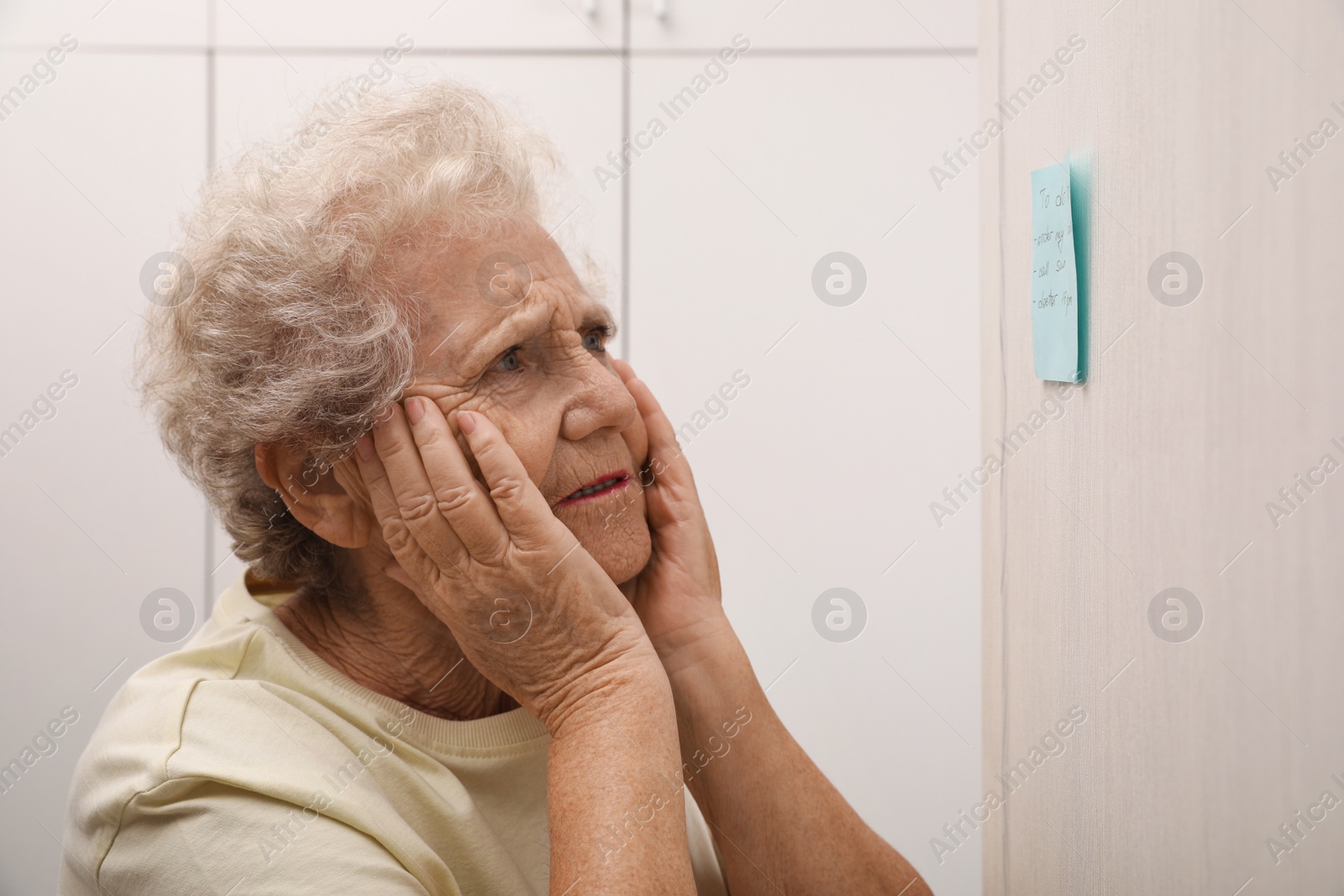 Photo of Senior woman looking at reminder note indoors. Age-related memory impairment