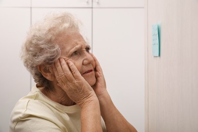 Photo of Senior woman looking at reminder note indoors. Age-related memory impairment