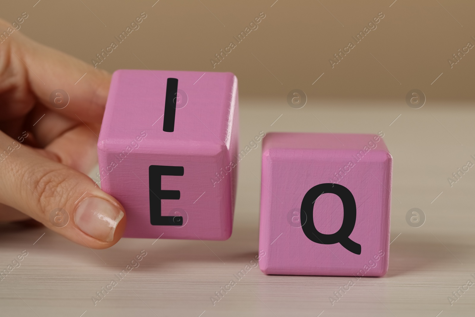 Photo of Woman turning pink cube with letters E and I near Q at white wooden table, closeup