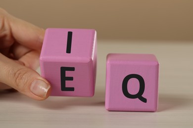 Woman turning pink cube with letters E and I near Q at white wooden table, closeup