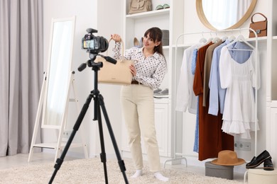 Photo of Smiling fashion blogger showing her bag while recording video at home