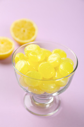 Tasty lemon drops in dessert bowl on violet background