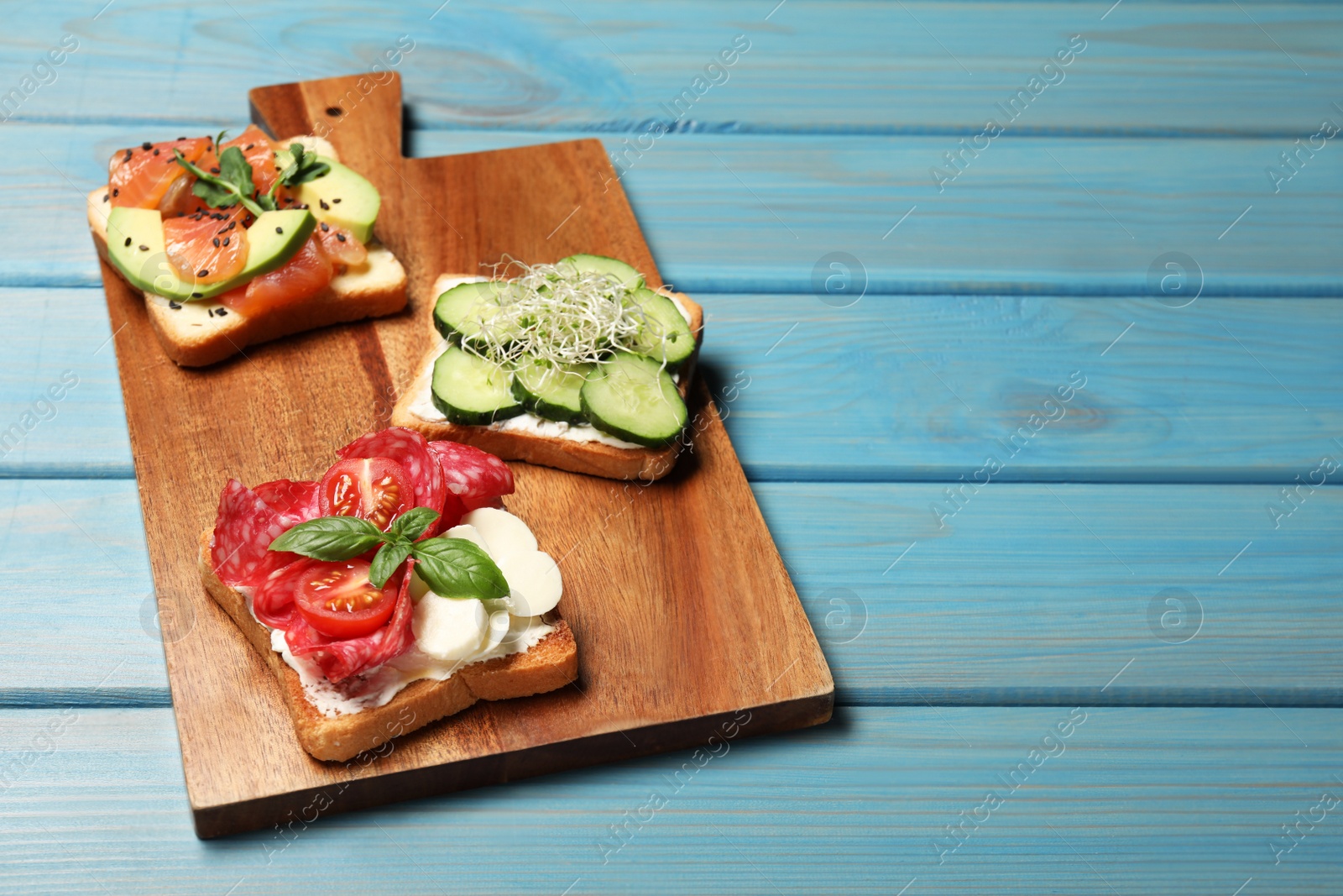 Photo of Tasty toasts with different toppings served on light blue wooden table. Space for text