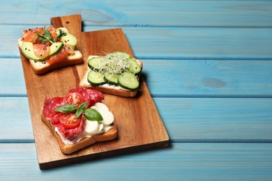 Tasty toasts with different toppings served on light blue wooden table. Space for text