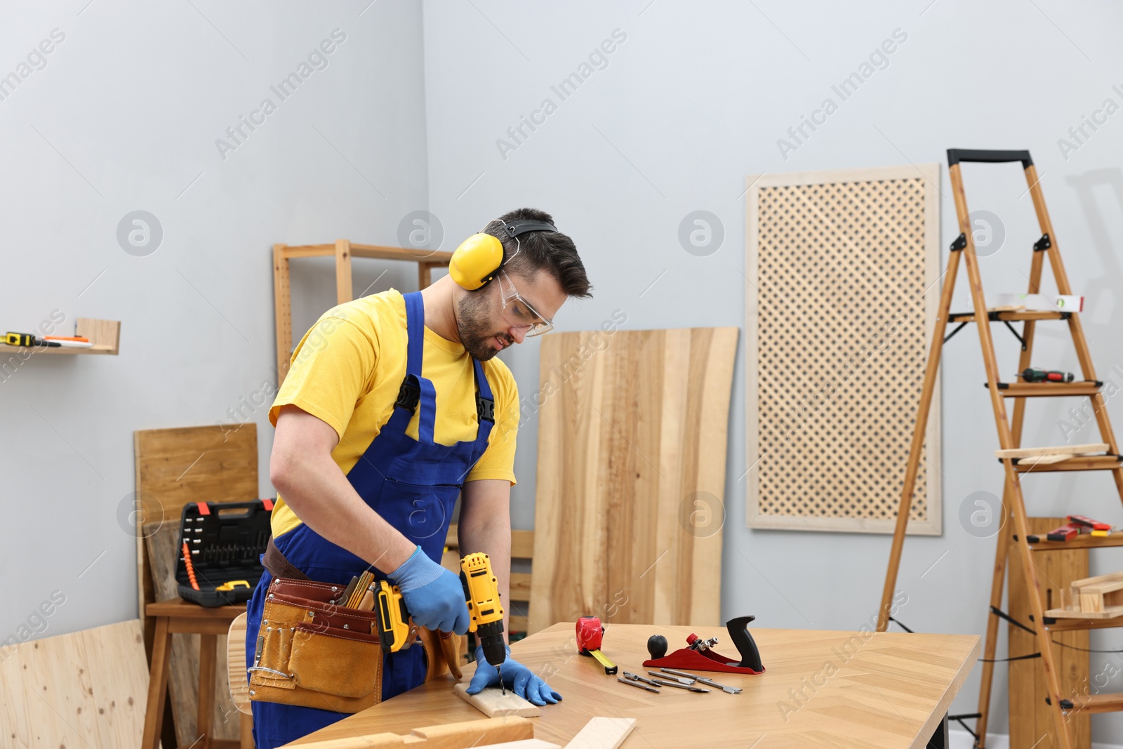 Photo of Young worker using electric drill at table in workshop