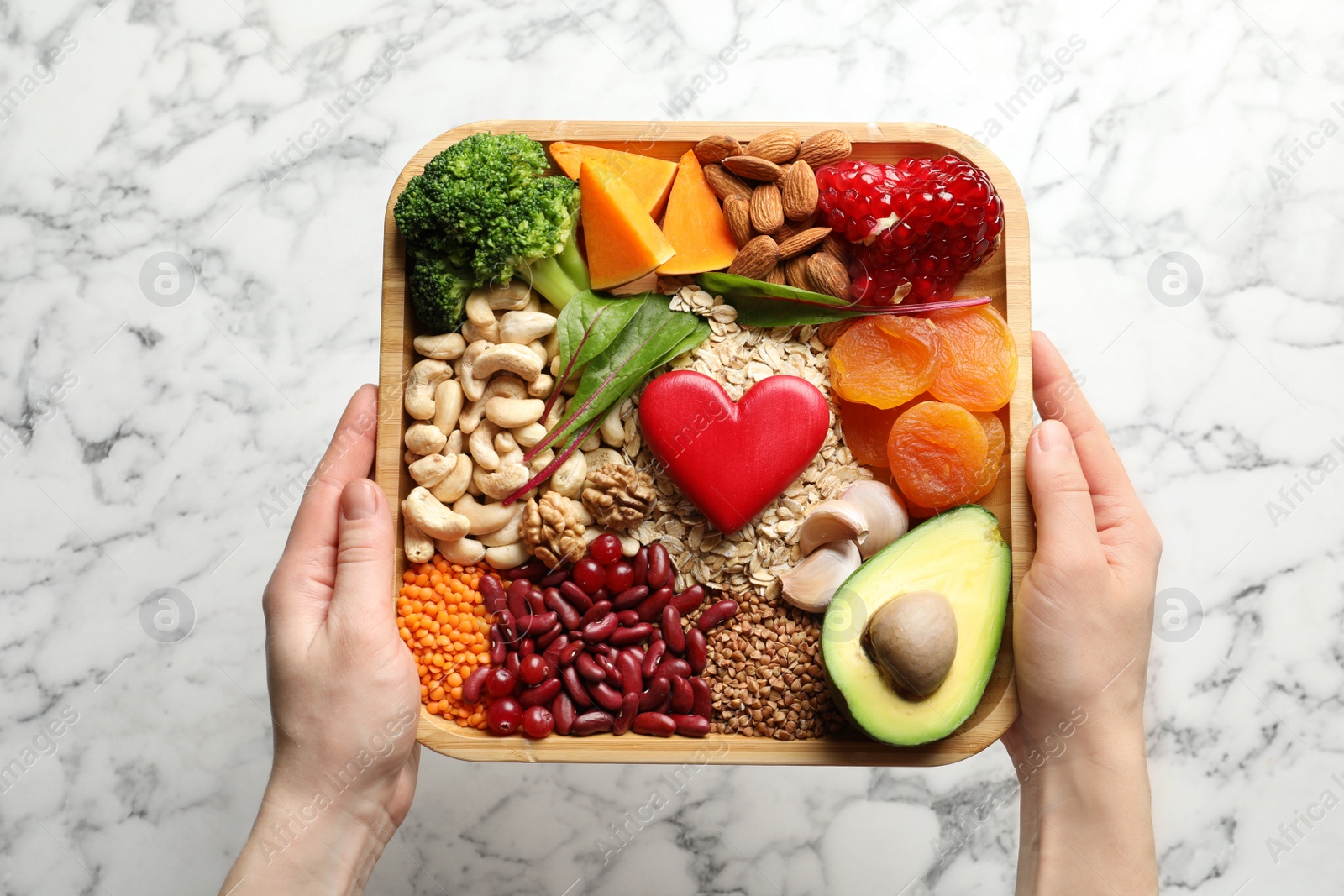 Photo of Woman holding wooden tray with heart-healthy products over table, top view