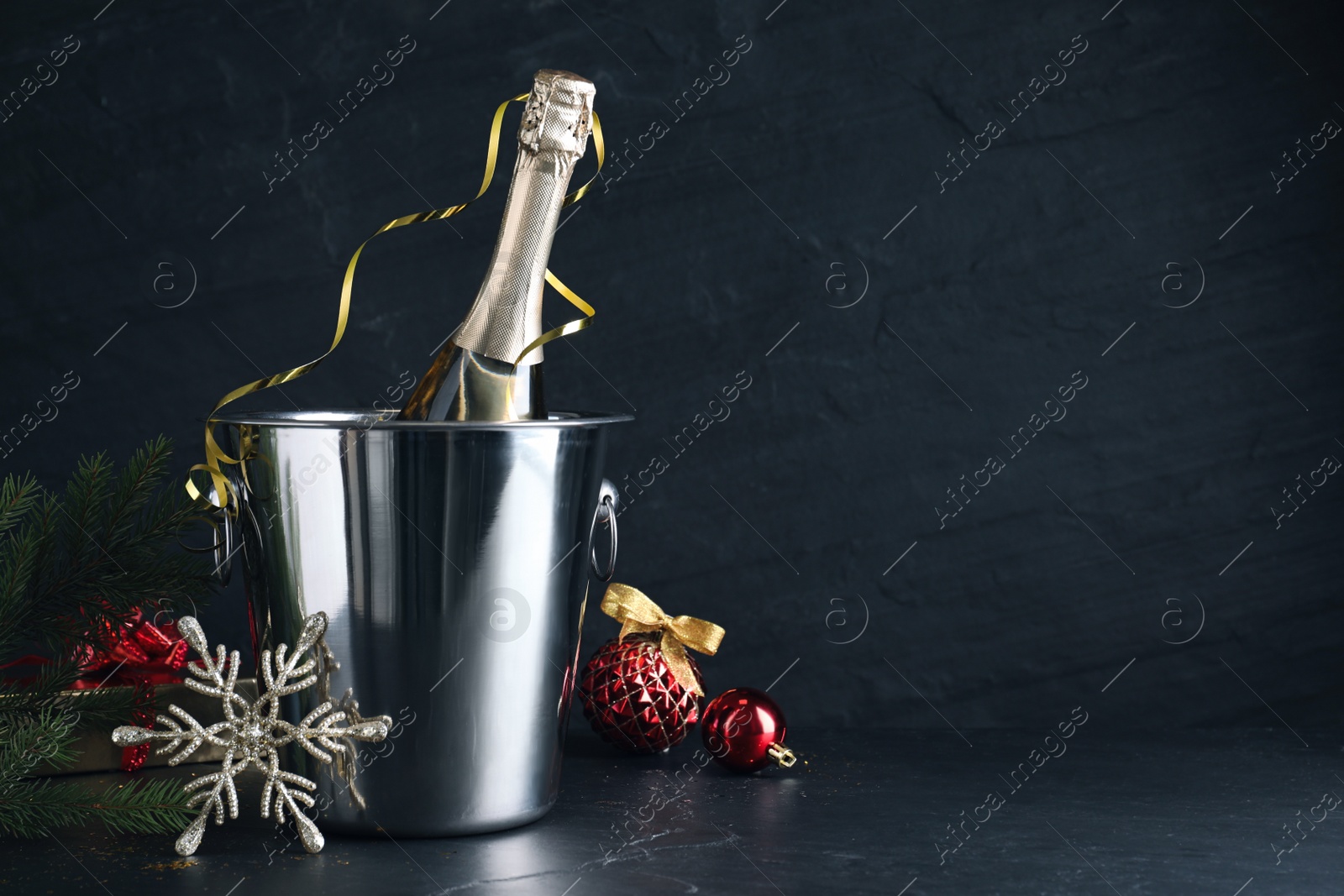 Photo of Happy New Year! Bottle of sparkling wine in bucket and festive decor on black background, space for text