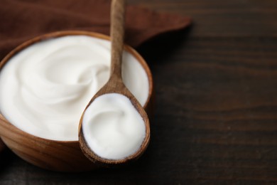 Delicious natural yogurt in bowl and spoon on wooden table, closeup. Space for text