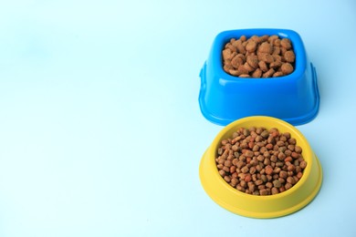 Photo of Dry pet food in feeding bowls on light blue background. Space for text