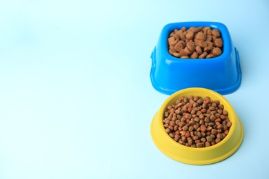 Dry pet food in feeding bowls on light blue background. Space for text