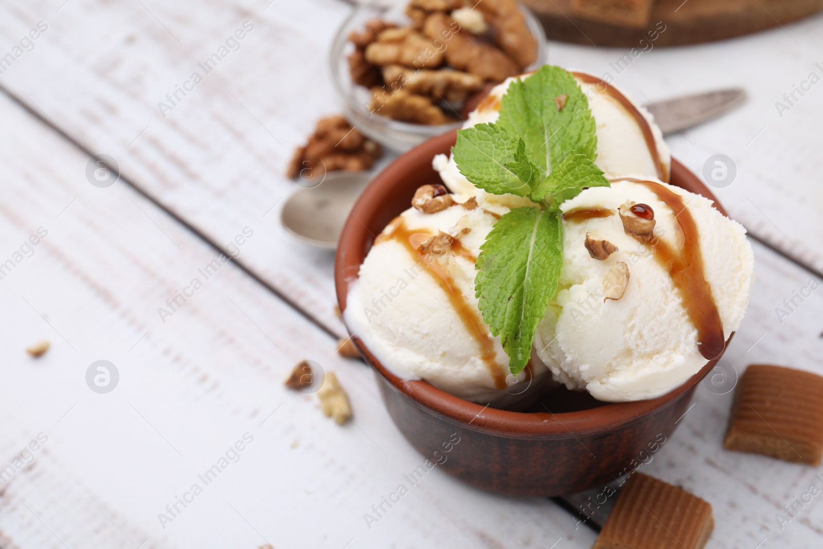 Photo of Bowl of tasty ice cream with caramel sauce, mint and nuts on white wooden table, closeup. Space for text