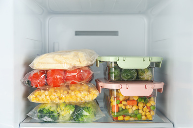 Plastic bags and containers with different frozen vegetables in refrigerator