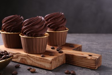 Photo of Delicious chocolate cupcakes and coffee beans on grey textured table, closeup. Space for text