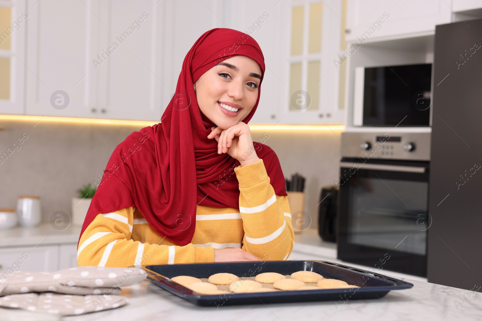 Photo of Portrait of Muslim woman near tray with cookies at white table in kitchen