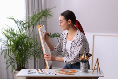 Photo of Happy woman artist drawing picture on canvas in studio