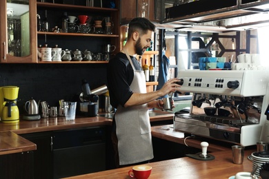 Photo of Barista frothing milk in metal pitcher with coffee machine steam wand at bar counter
