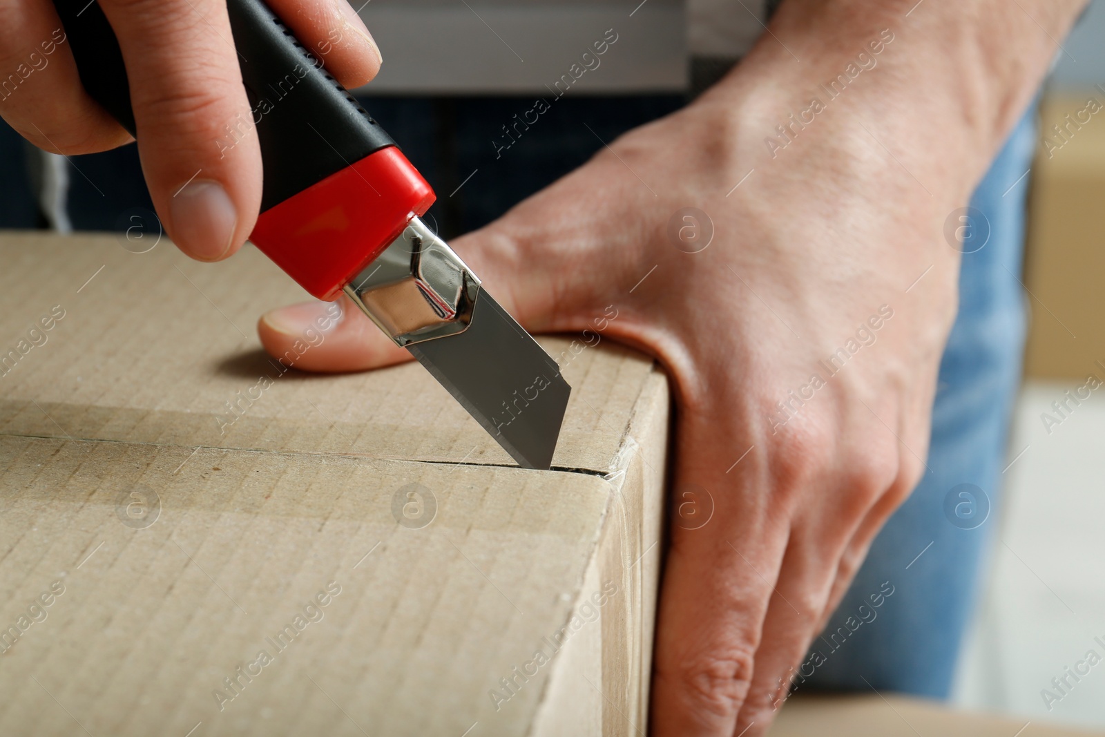 Photo of Man using utility knife to open parcel, closeup