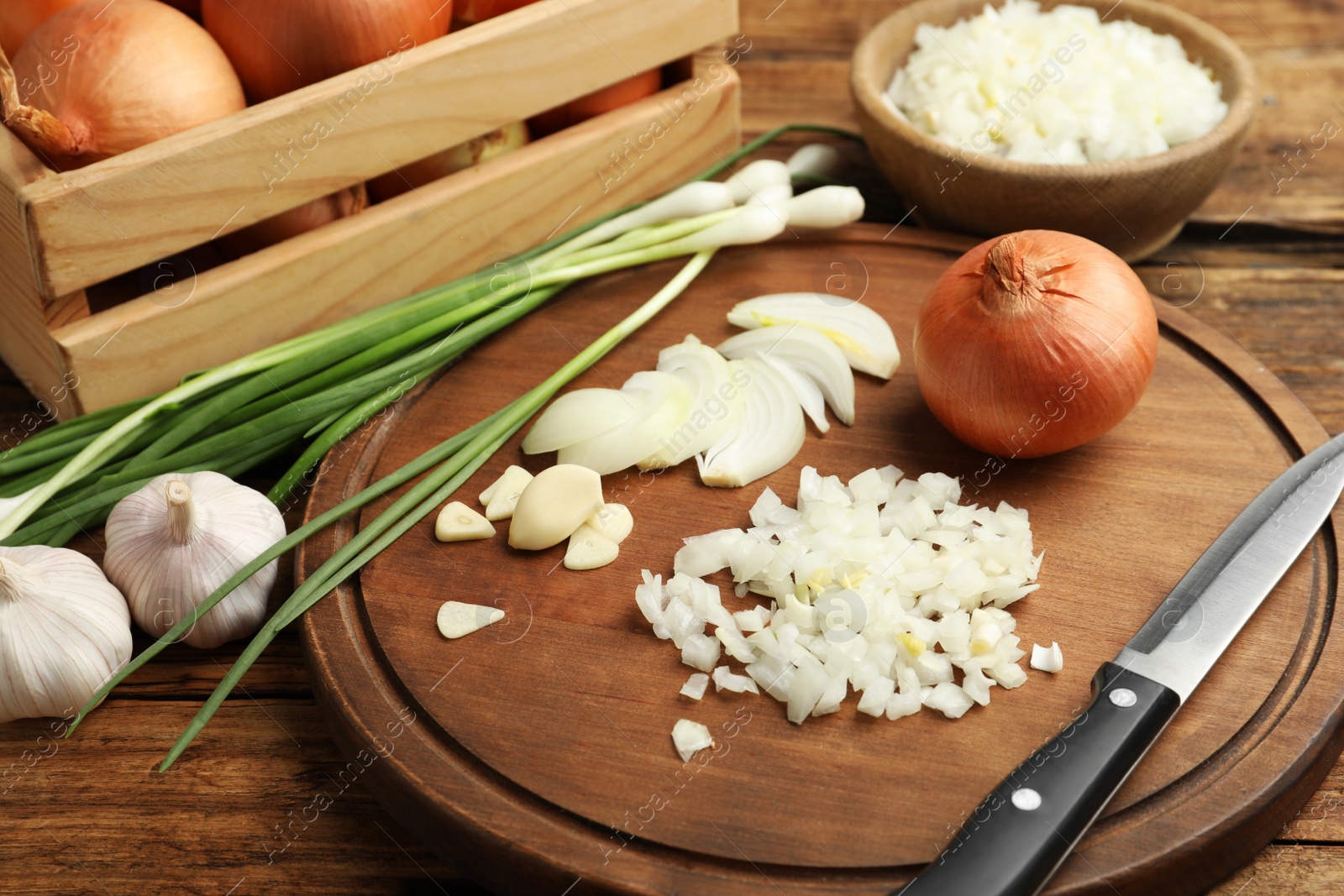 Photo of Board with cut onion and garlic on wooden table