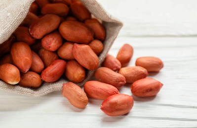 Photo of Fresh peanuts in sack on white wooden table, closeup