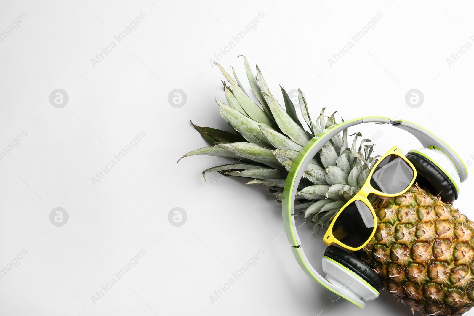 Photo of Pineapple with sunglasses and headphones on white background, top view. Creative concept