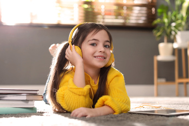 Photo of Cute little girl with headphones listening to audiobook at home