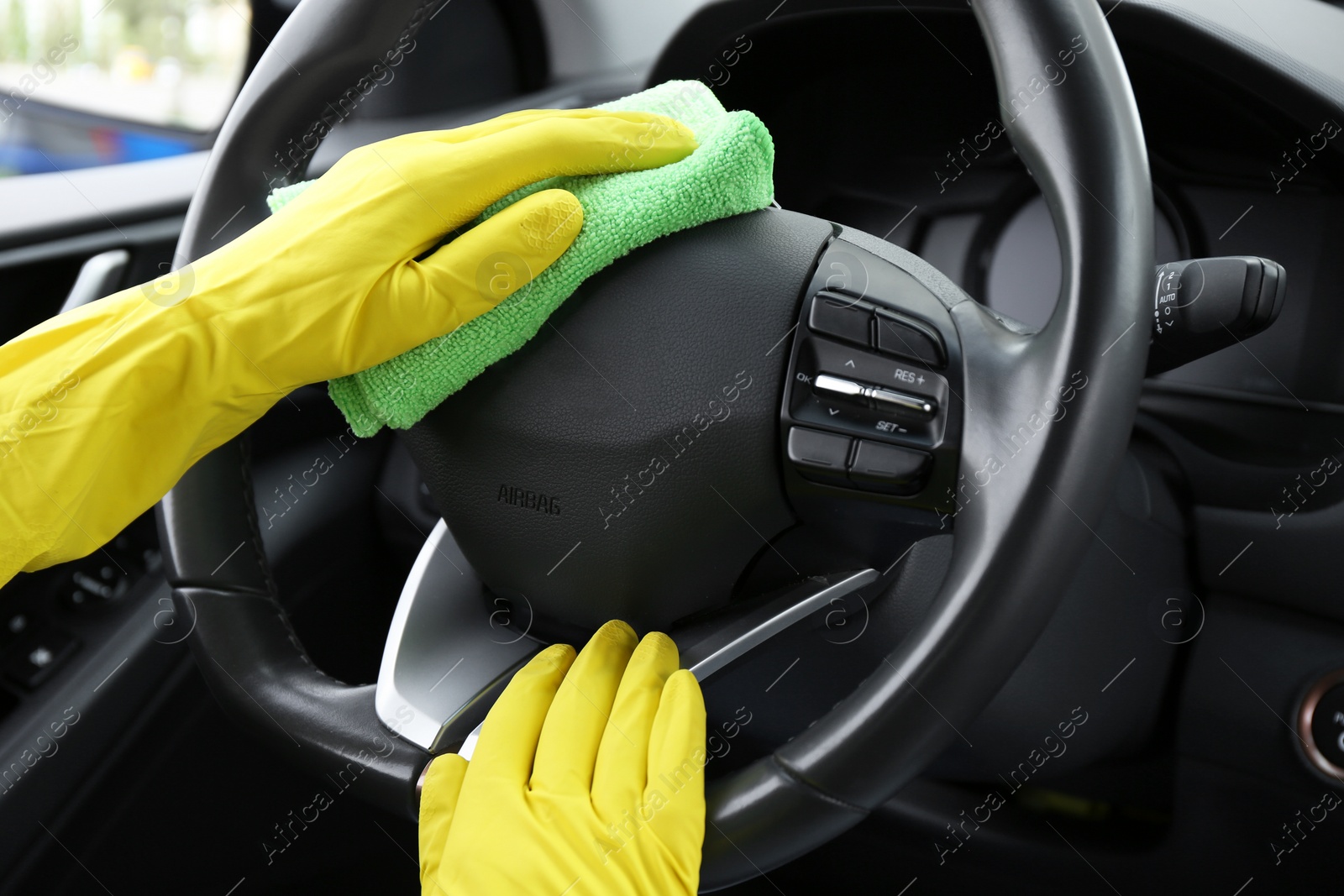 Photo of Woman cleaning steering wheel with rag in car, closeup