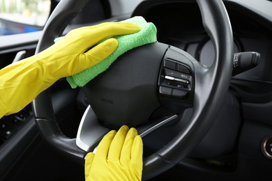 Woman cleaning steering wheel with rag in car, closeup