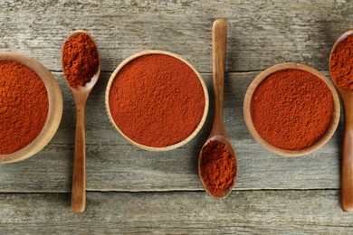 Photo of Bowls and spoons of paprika on wooden table, flat lay