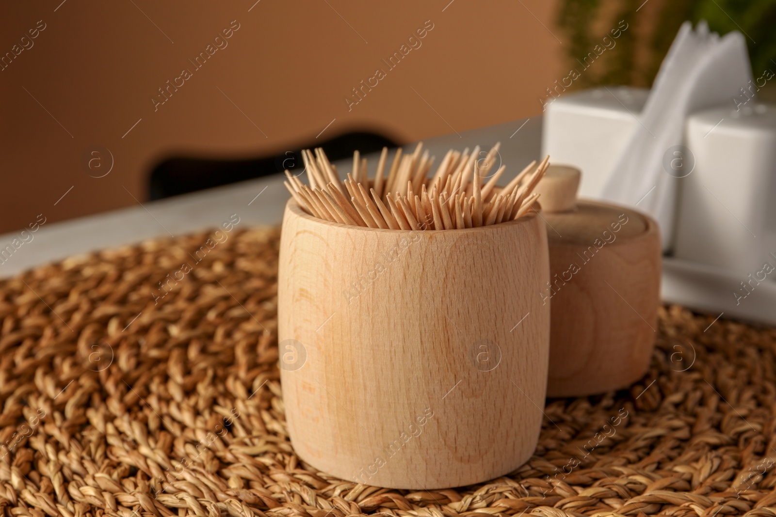 Photo of Wooden holder with many toothpicks on wicker mat, closeup. Space for text