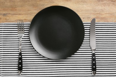 Photo of Empty plate, fork and knife on wooden table, flat lay