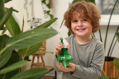 Photo of Cute little boy spraying beautiful green plant at home. House decor