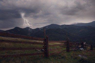 Image of Dark cloudy sky with lightnings over mountain countryside with wooden fence. Thunderstorm