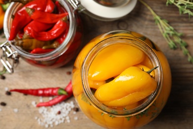 Glass jars with pickled peppers on wooden table, flat lay