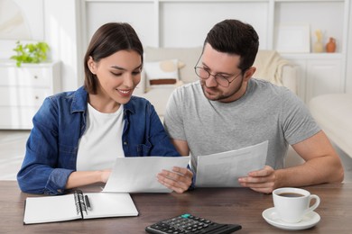Photo of Young couple with papers discussing pension plan at wooden table indoors