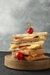 Photo of Stack of tasty sandwiches with ham and melted cheese served with tomatoes on black textured table