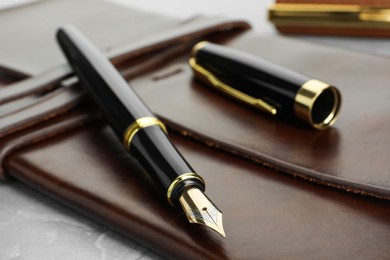 Photo of Stylish fountain pen, cap and leather notebook on light grey table, closeup
