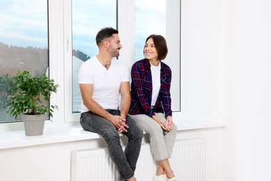 Photo of Happy couple sitting on windowsill in new apartment. Moving day