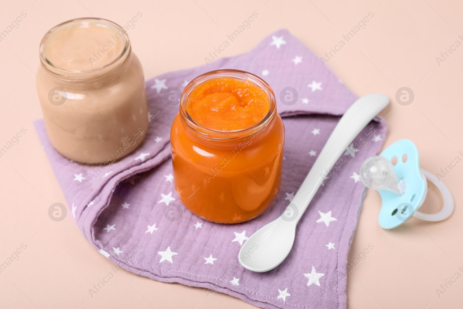 Photo of Healthy baby food, spoon and pacifier on pale pink background