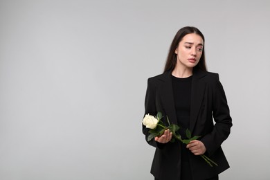 Photo of Sad woman with white rose flowers on light grey background, space for text. Funeral ceremony