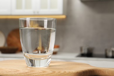 Photo of Filtered water in glass on board in kitchen, closeup. Space for text