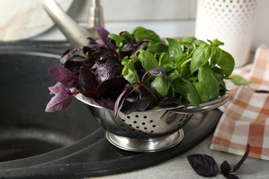 Photo of Metal colander with different fresh basil leaves on sink