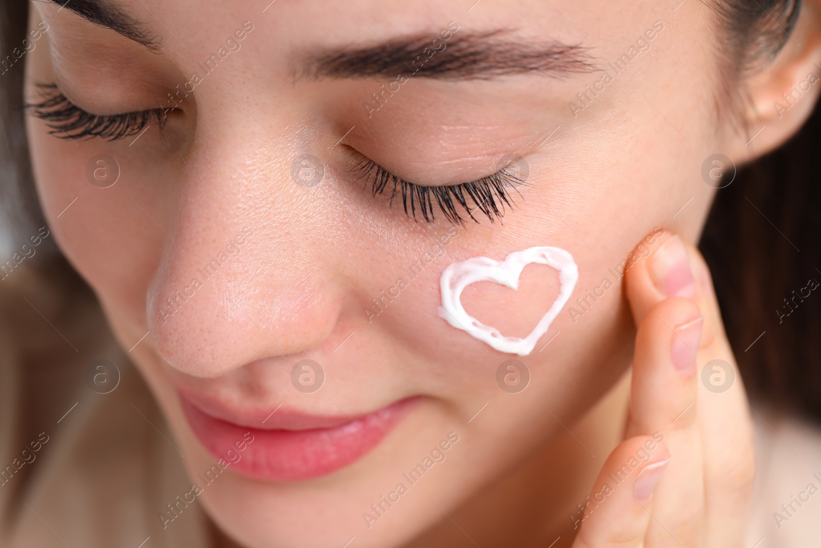 Photo of Young woman with dry skin and heart made of cream on her face, closeup